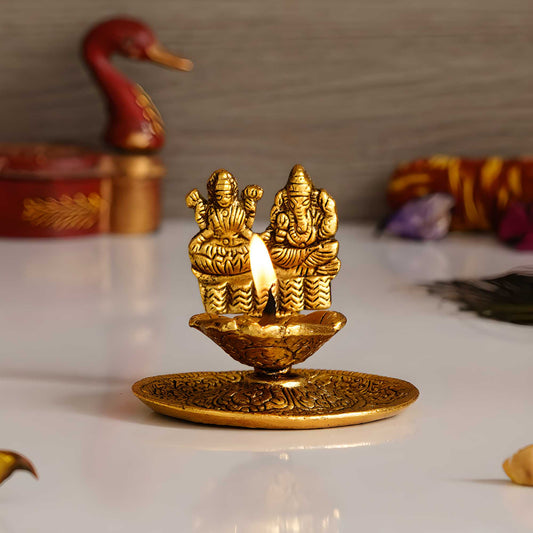 Gold-colored diya with two figures on a white surface